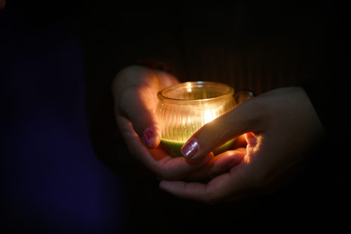 hands holding lit candle in the dark
