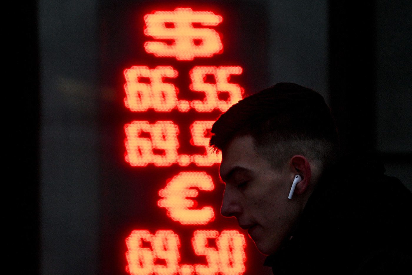 man wearing airpods silhouetted against black screen with red currencies on it