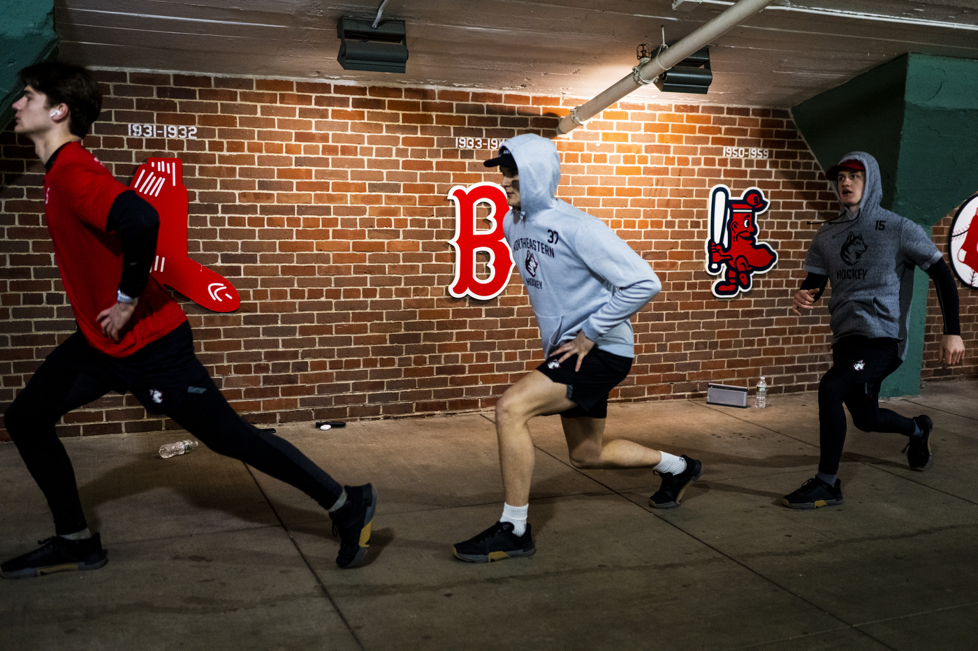 Three people are running through a hall at Fenway Park. 