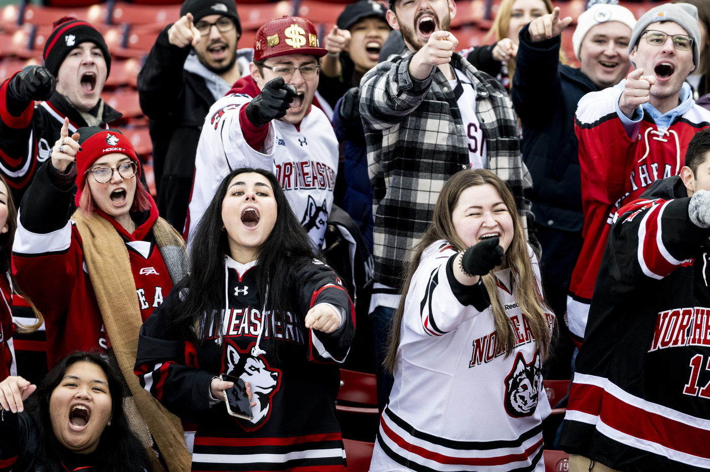 A group of people wearing Northeastern merchandise cheer on the university's hockey team. 