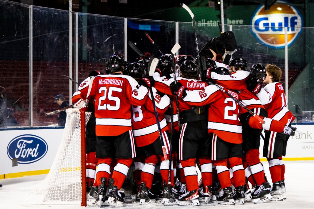 Hockey players in red uniforms gather around their goalie.