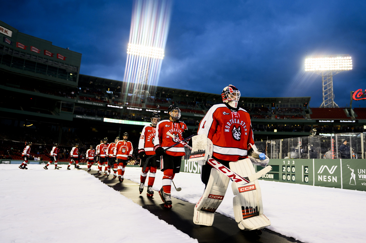 A row of Northeastern hockey players walking over to an ice skating rink in Fenway Park. 