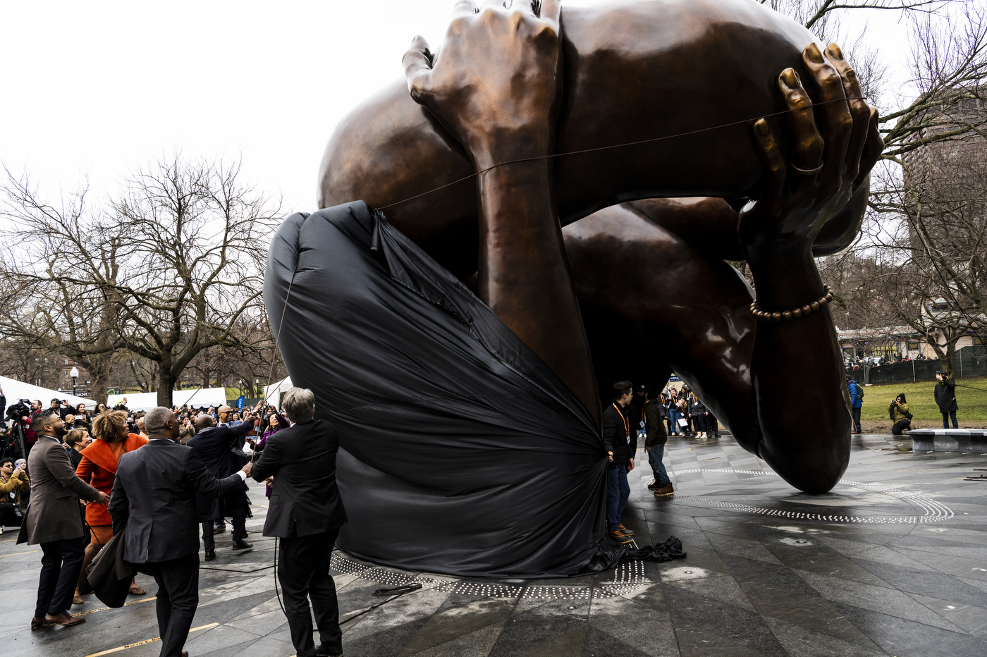 several people pull a black tarp down to reveal the embrace statue