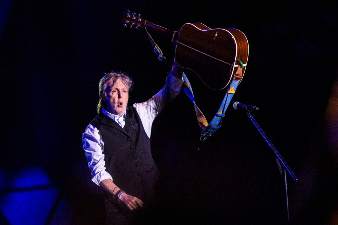 Paul McCartney on stage, lifting his guitar