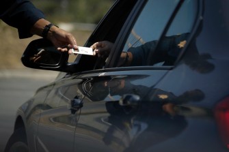 driver handing their ID to a police officer through the window of their car