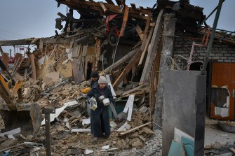 person carrying belongings out of a bombed home