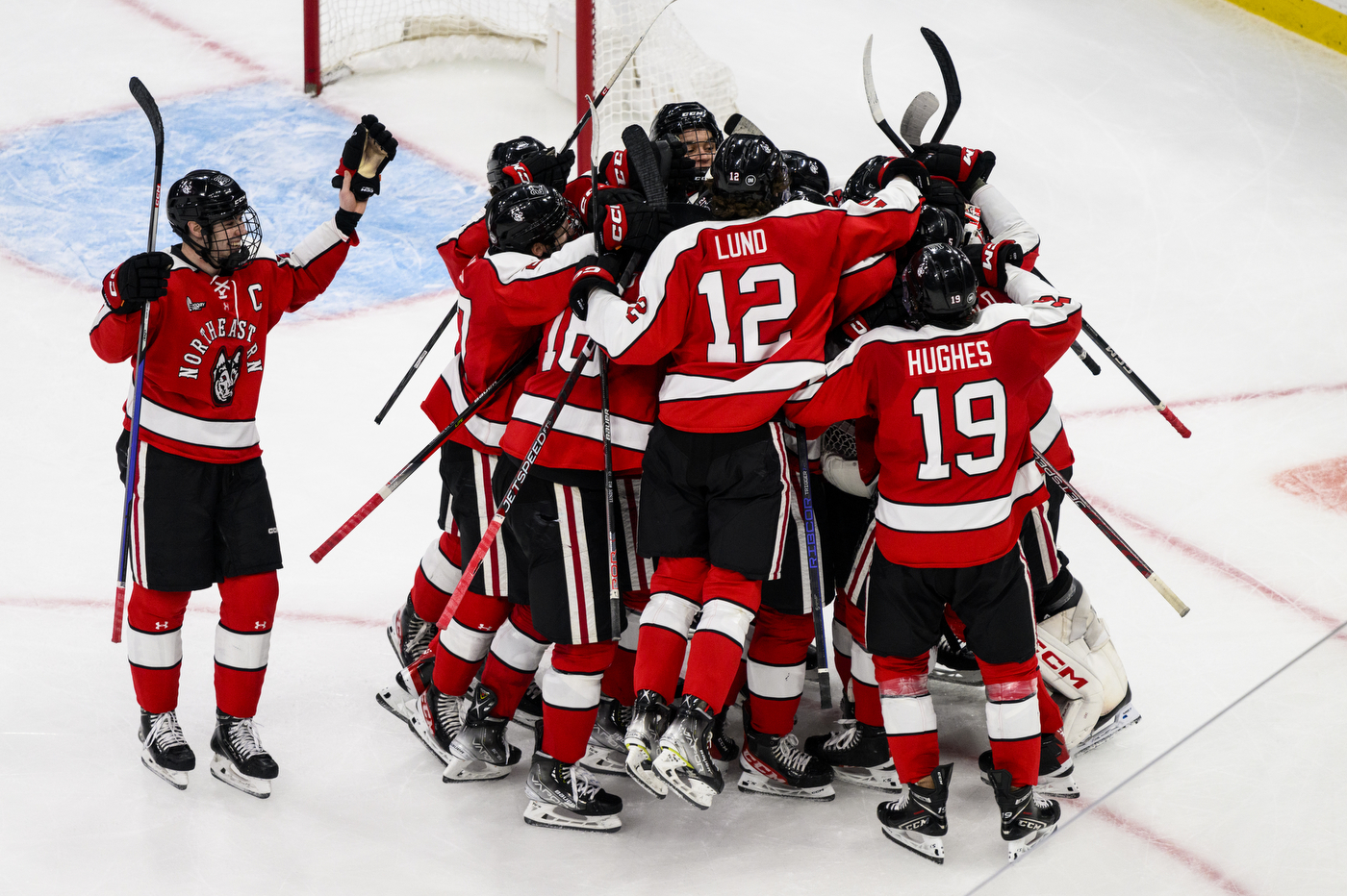 A group of Northeastern hockey players celebrate a win together on the ice.