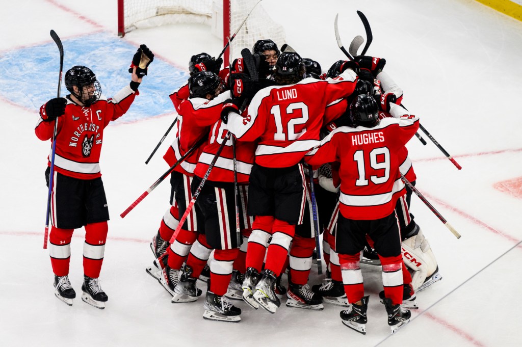 A group of Northeastern hockey players celebrate a win together on the ice.