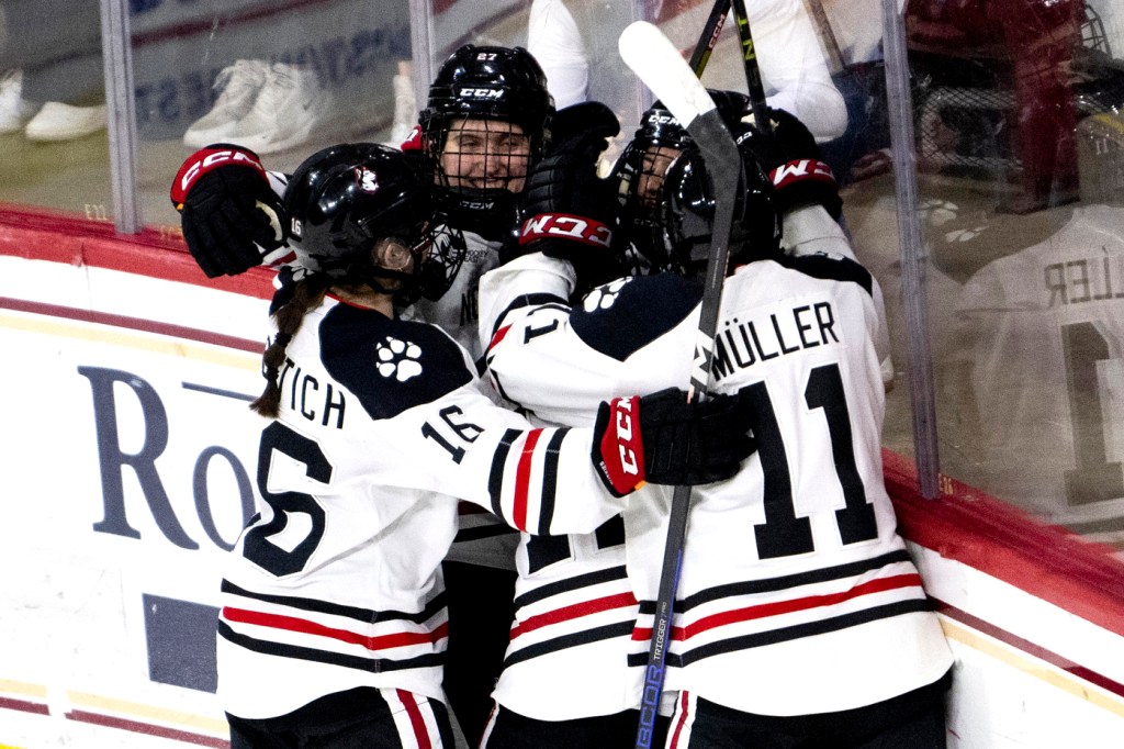group of players from northeastern womens hockey team hugging in celebration