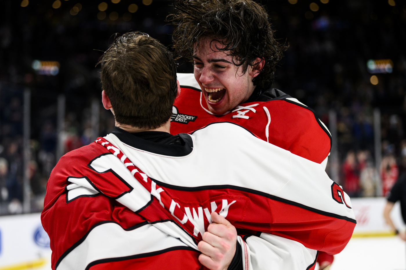 two northeastern hockey players jump into each others arms in celebration