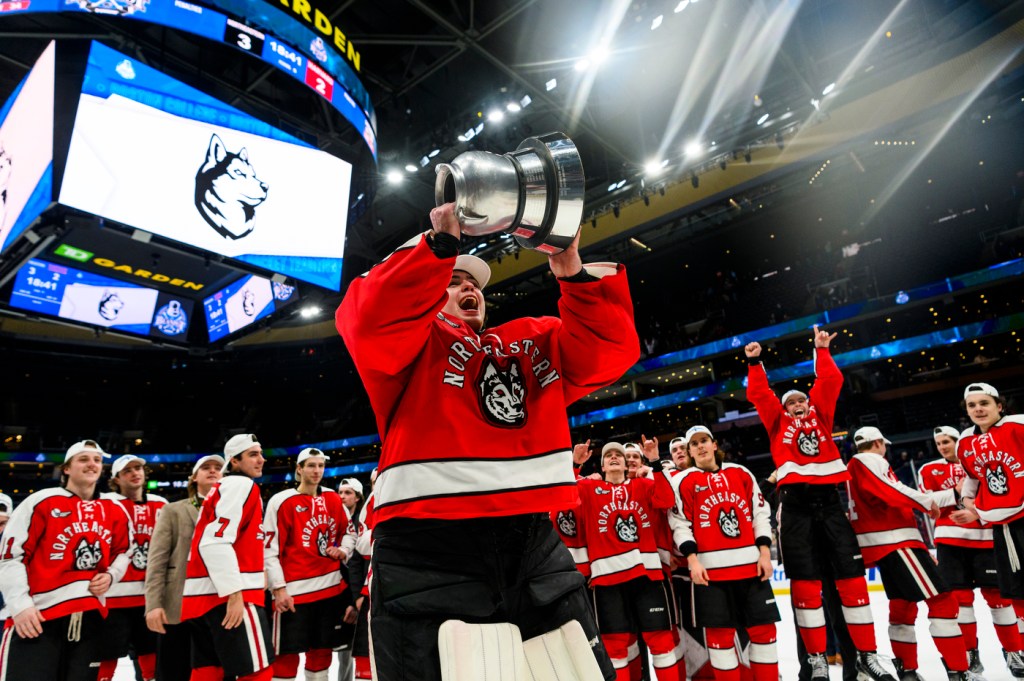 northeastern mens hockey player holds the beanpot trophy up in celebration