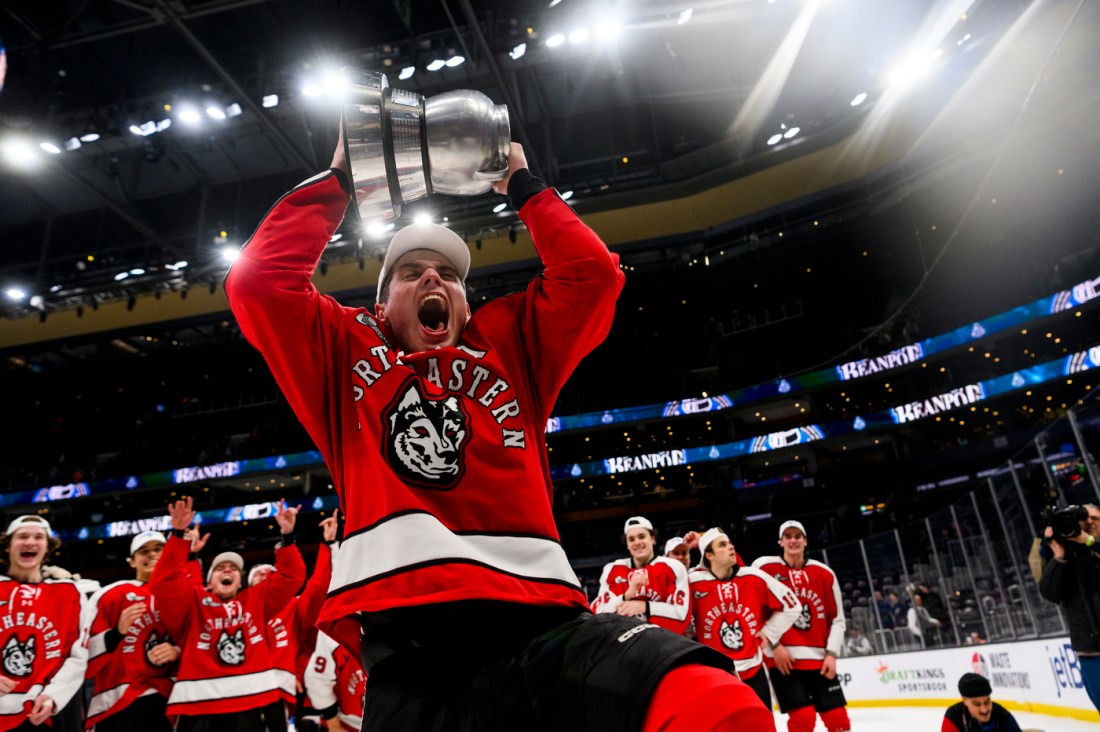 Member of the Northeastern community holding up the beanpot trophy and cheering. 