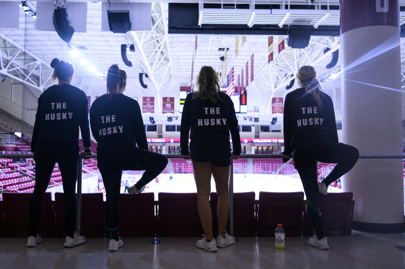 four players stand and stretch while overlooking an empty ice hockey arena