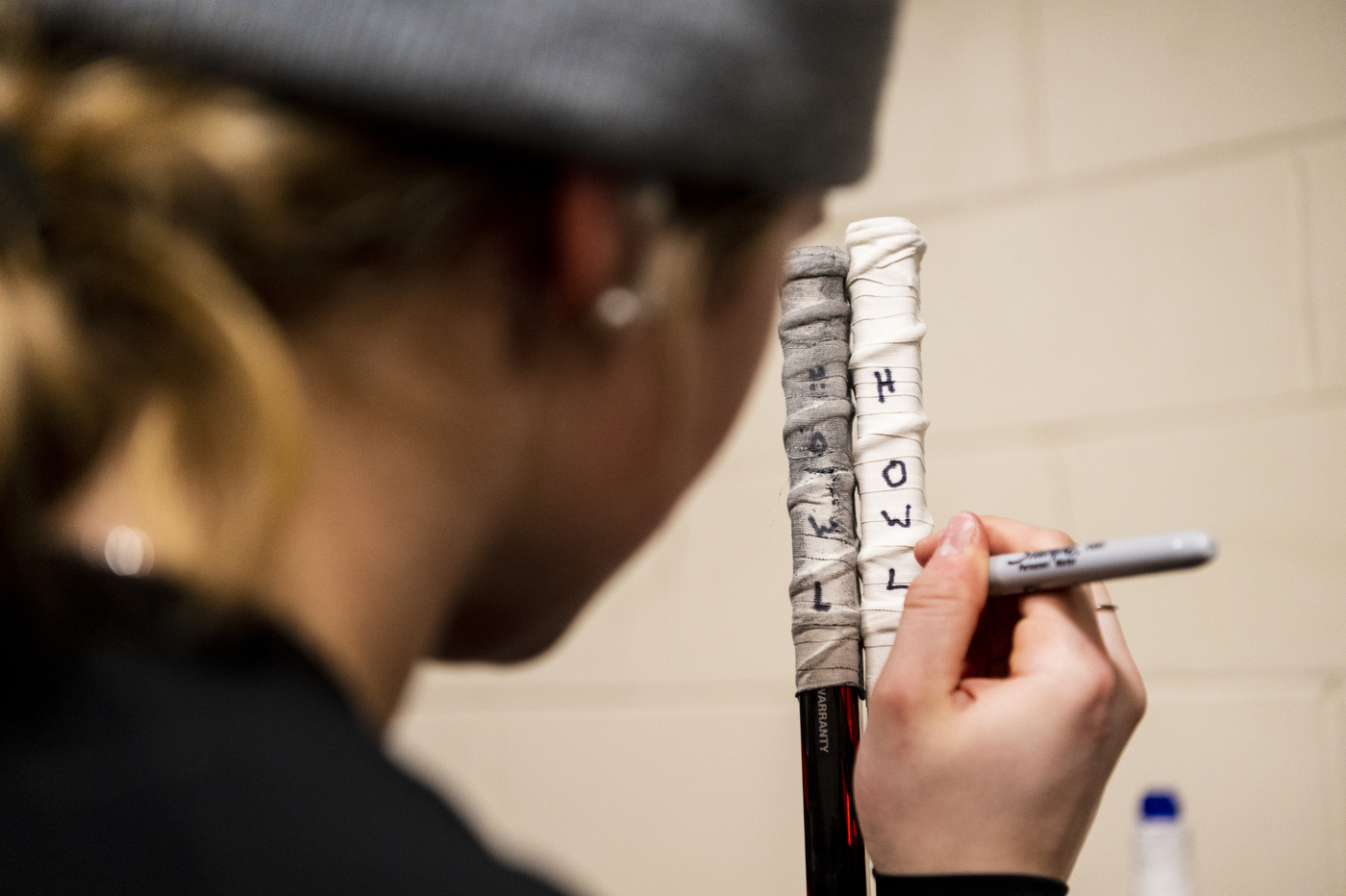 A player uses a marker to write 'howl' on tape wrapped around the top of a hockey stick