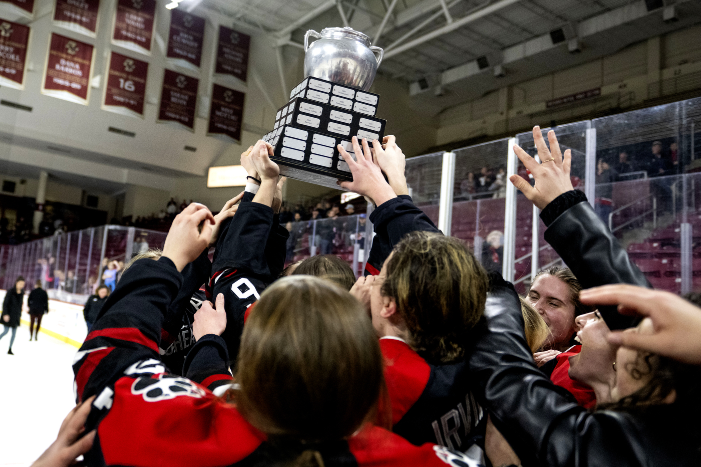 A crowd of players reaches up to touch the Beanpot trophy as it held above their heads. 