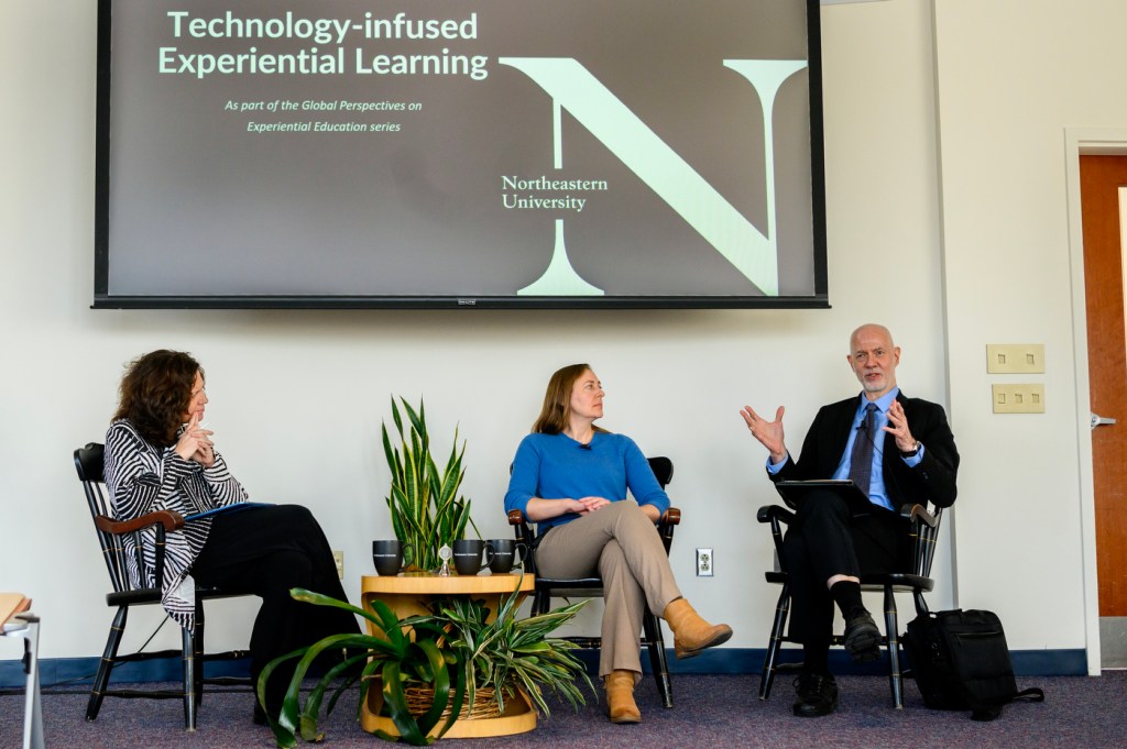 Three people sitting underneath a projector screen having a panel conversation