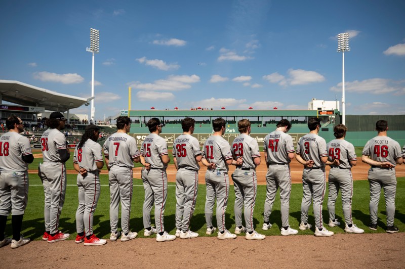 Baseball players stand in line on the field with their hands over their hearts 
