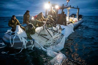 Sailors on a boat lit by spotlights at night recover a high-altitude surveillance balloon from the ocean.