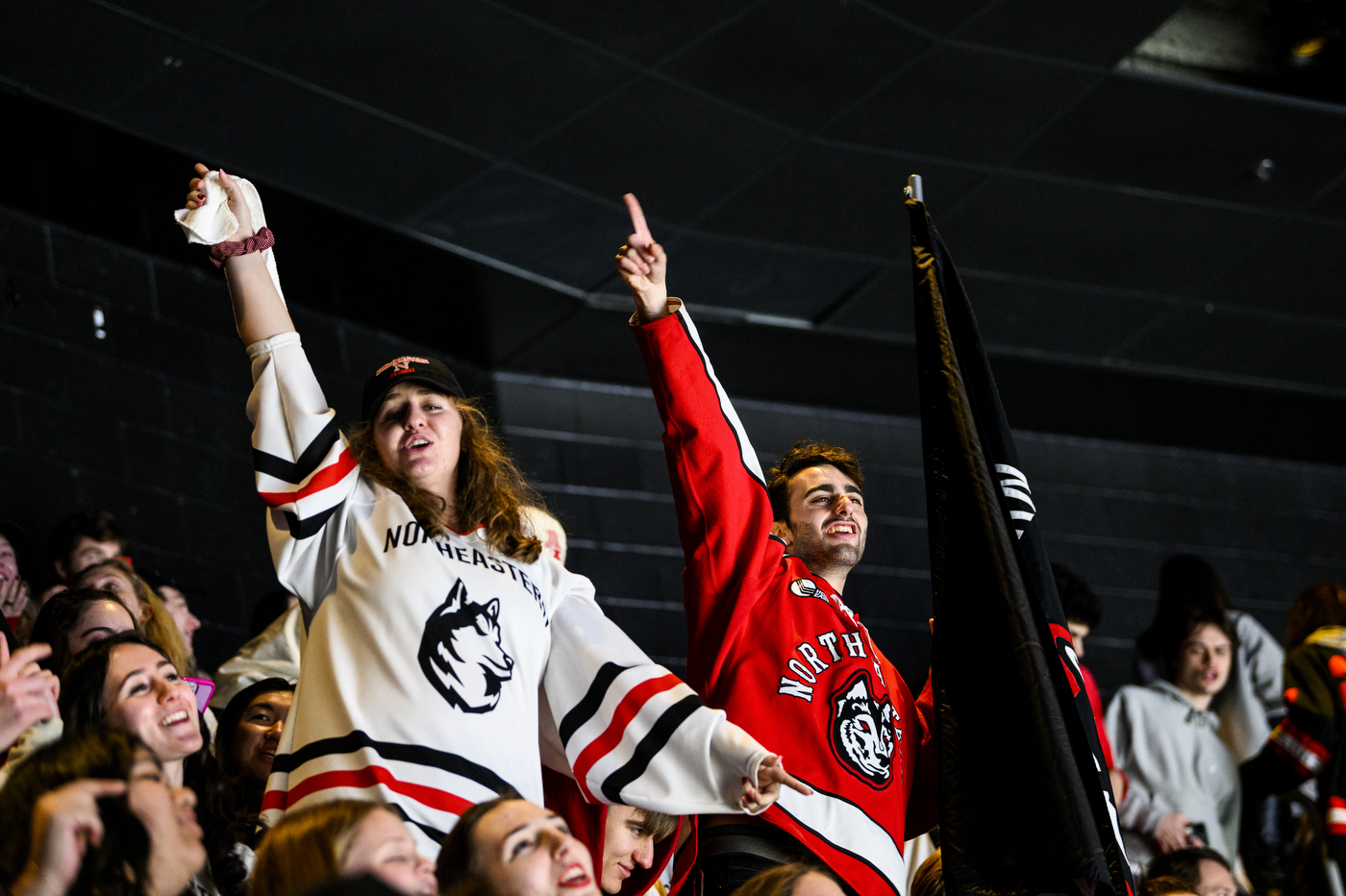 two people wearing Northeastern hockey cheers hold their right hands in the air