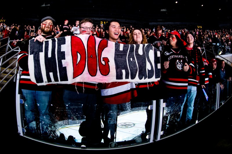 northeastern hockey fans holding a poster that says the dog house on it
