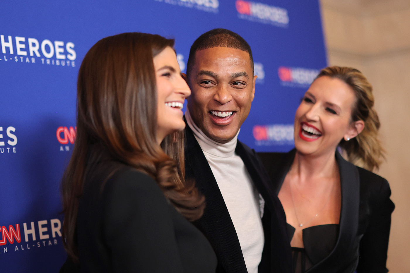 Kaitlan Collins, Don Lemon, and Poppy Harlow smile at eachother in front of a step and repeat