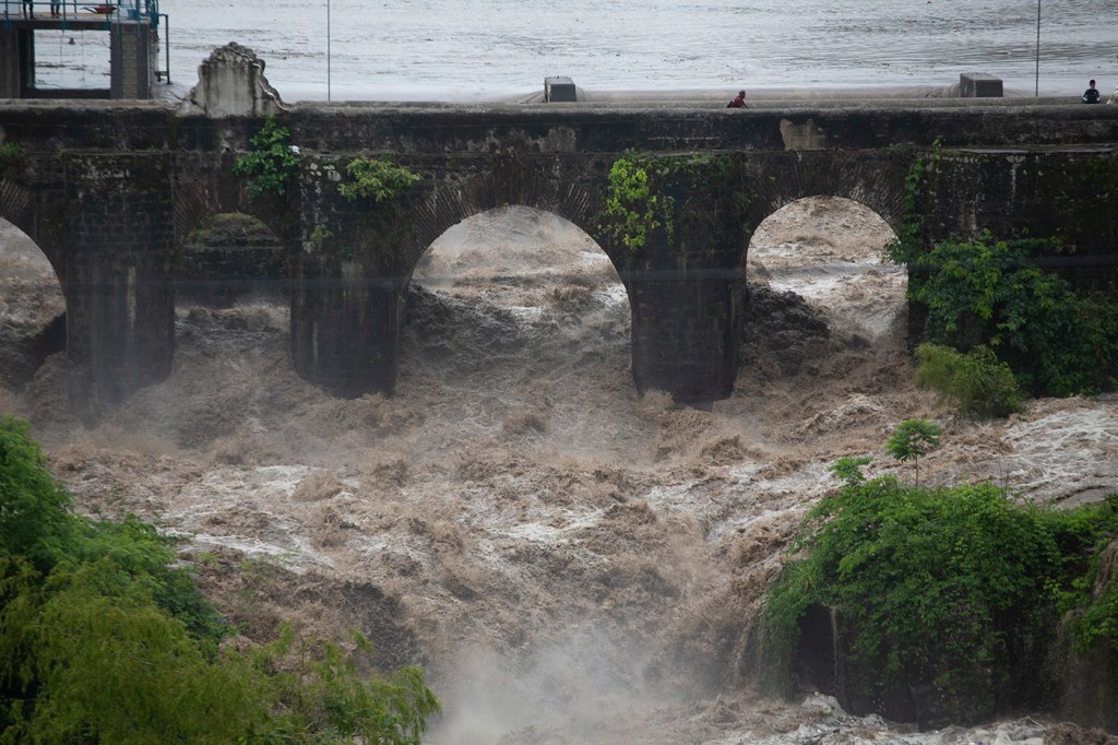 A violently overflowing river rushes under a bridge.