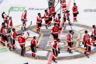 Northeastern players in red uniforms gather on the Bruins ice logo at TD Garden