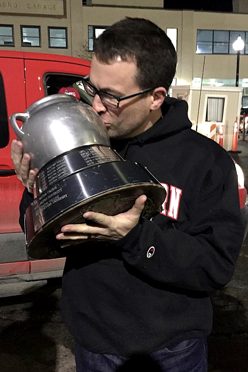 person wearing northeastern sweatshirt kissing beanpot trophy