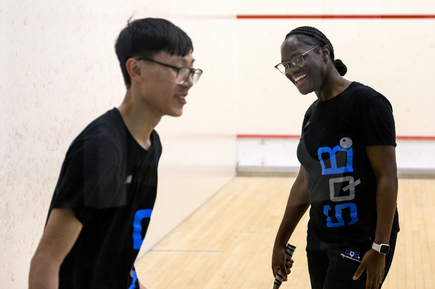 two young people wearing SquashBusters shirts inside a squash court