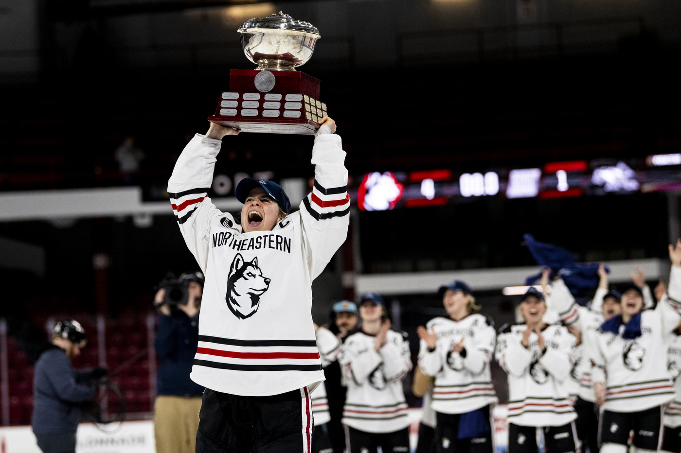 A women's hockey player lifts trophy overhead