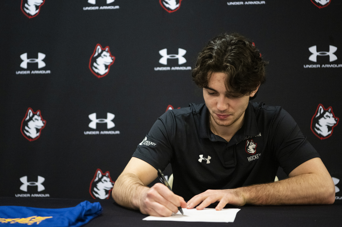 Devon seated in front of a Huskies backdrop, signing the contract