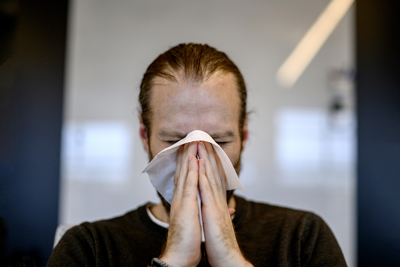 person blowing their nose due to seasonal allergies