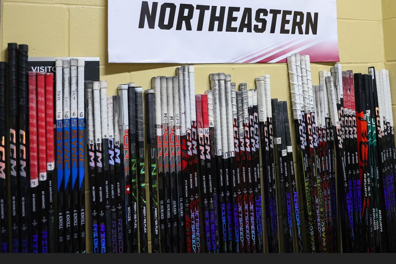 line of hockey sticks leaning up against the wall