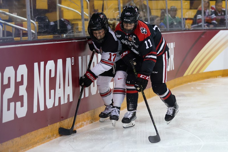 a northeastern and ohio hockey player each battle for the puck