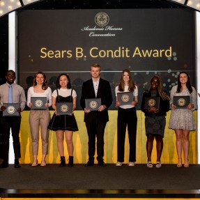 Students pose on a stage while holding awards