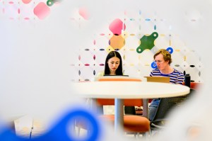Two students work on a project near a colorful background.
