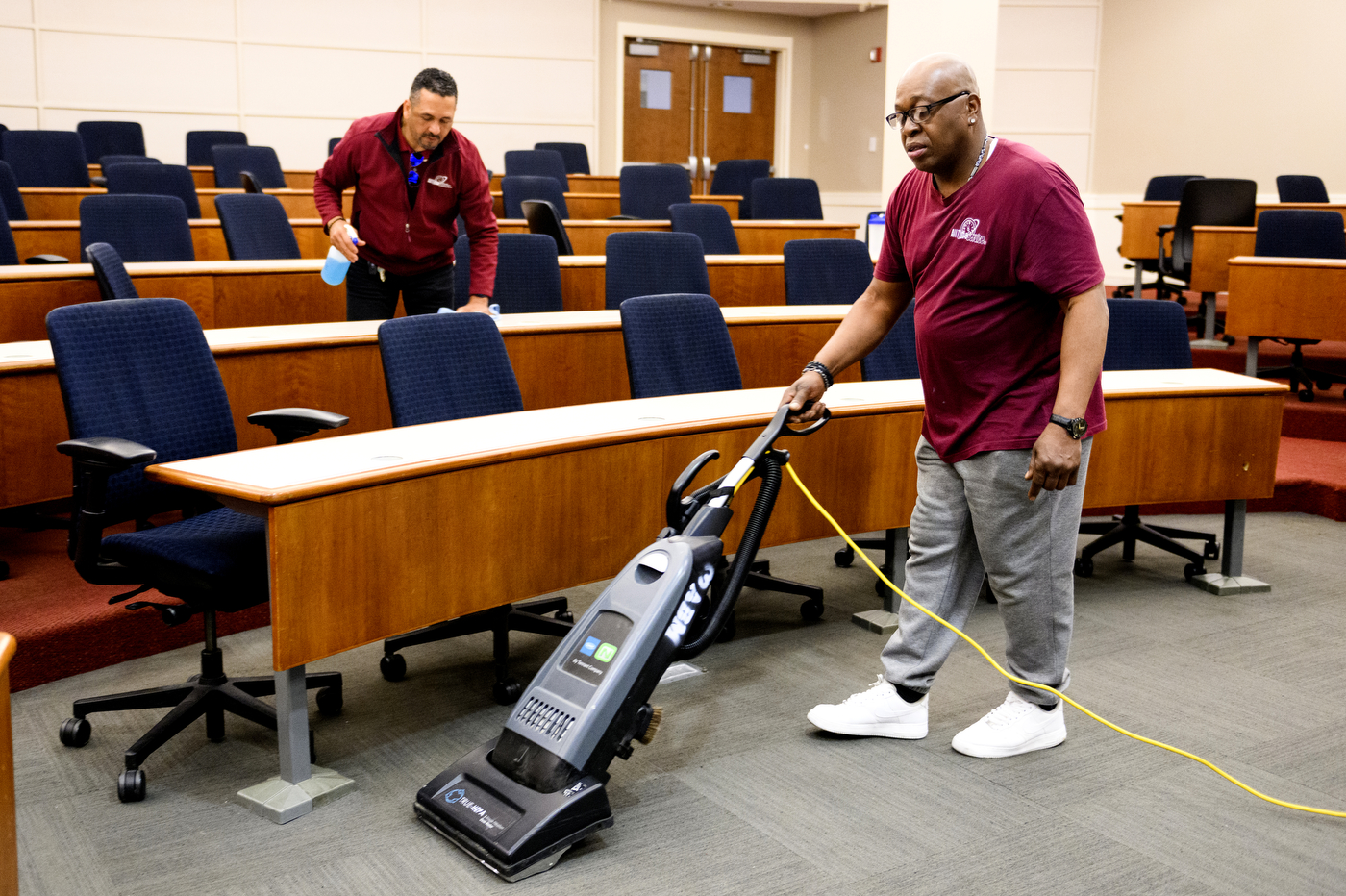 Someone wiping down desks while another person vacuums