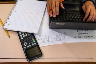 Student's hands typing on laptop as they complete homework with a notebook and calculator on the desk next to them