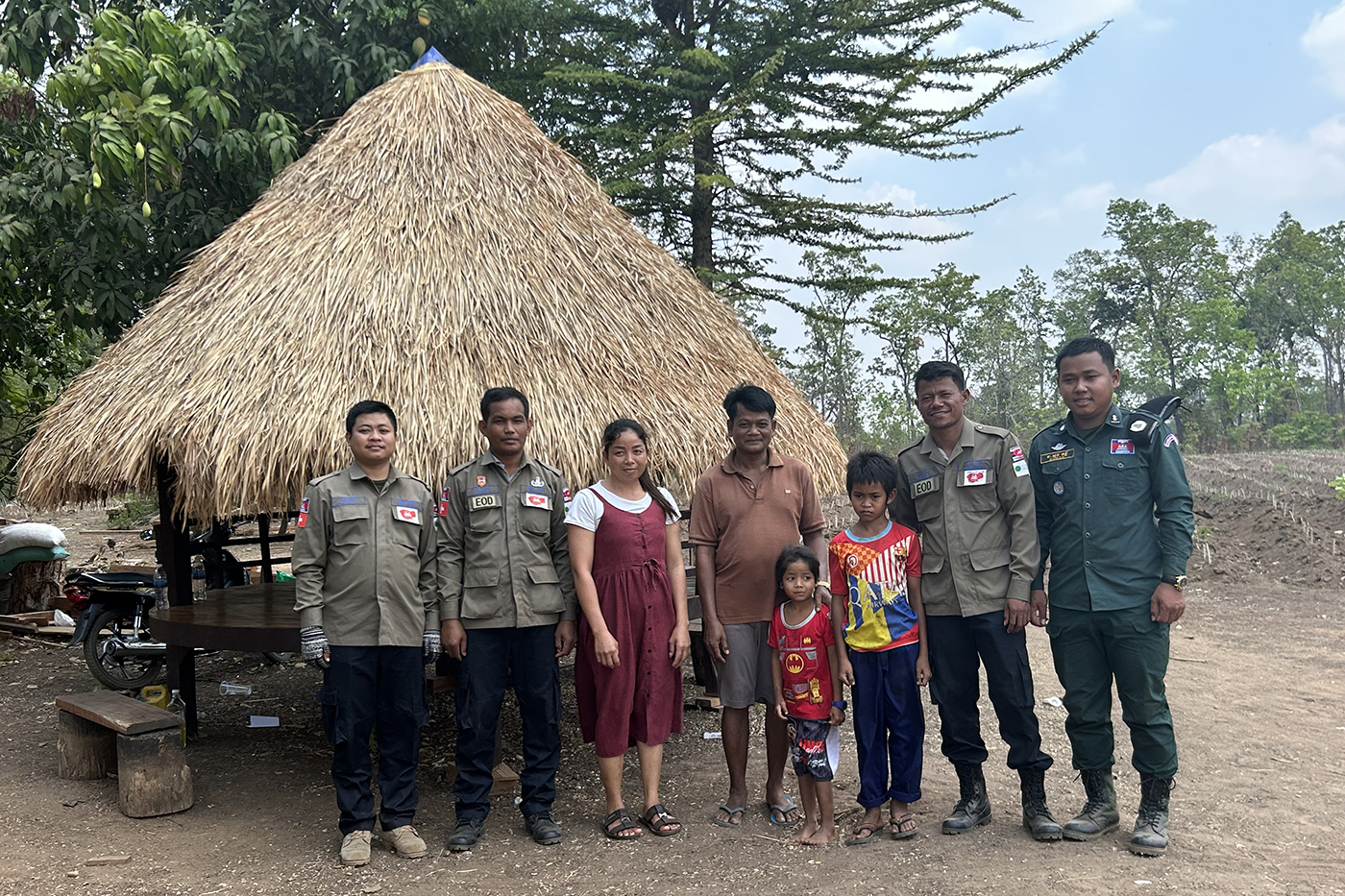 co-op student posing with Cambodians in front of a hut with a straw roof