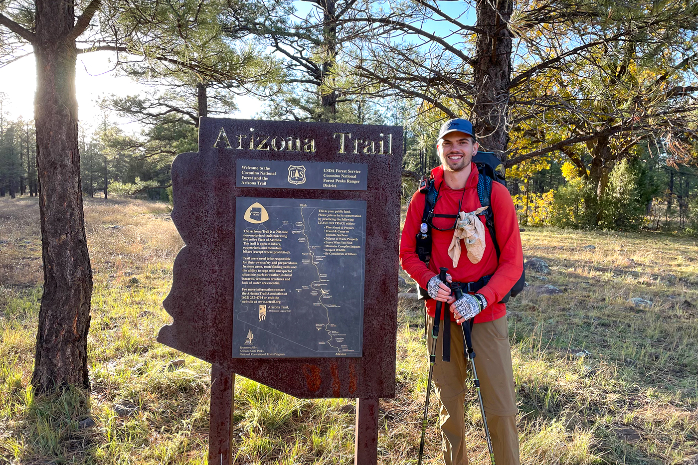 Michael Nelson stands with hiking poles in front of an Arizona Trail sign.