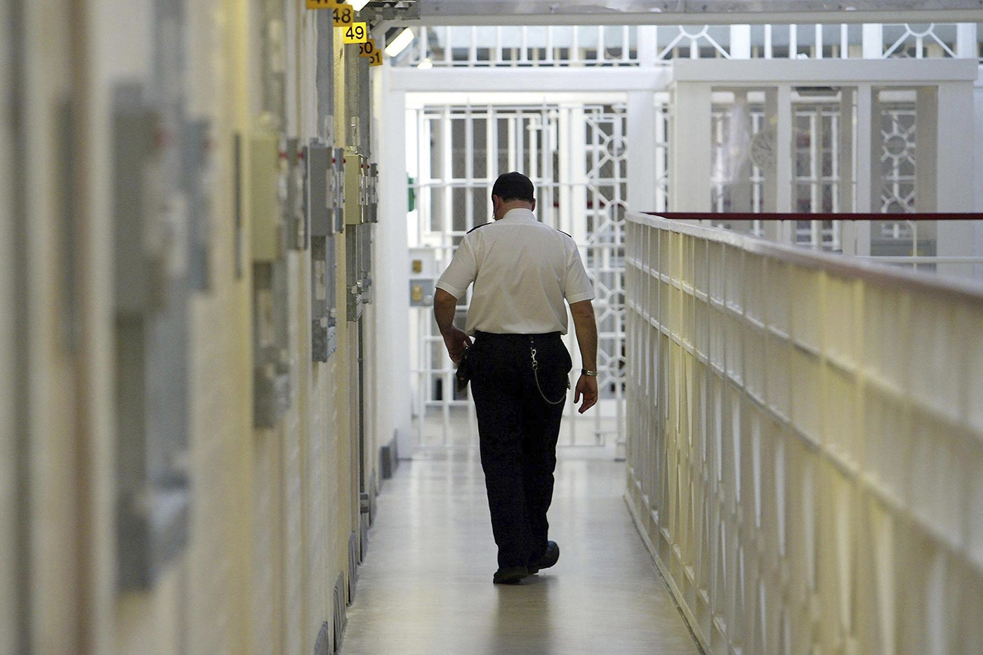Prison guard walks down a hallway of cells.