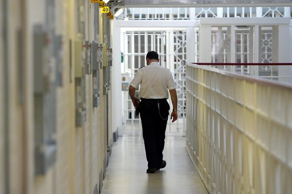 Prison guard walks down a hallway of cells.