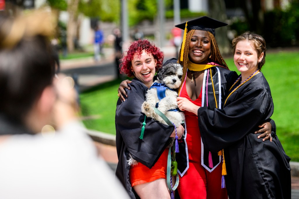 Three graduates pose for a photo while holding a dog.