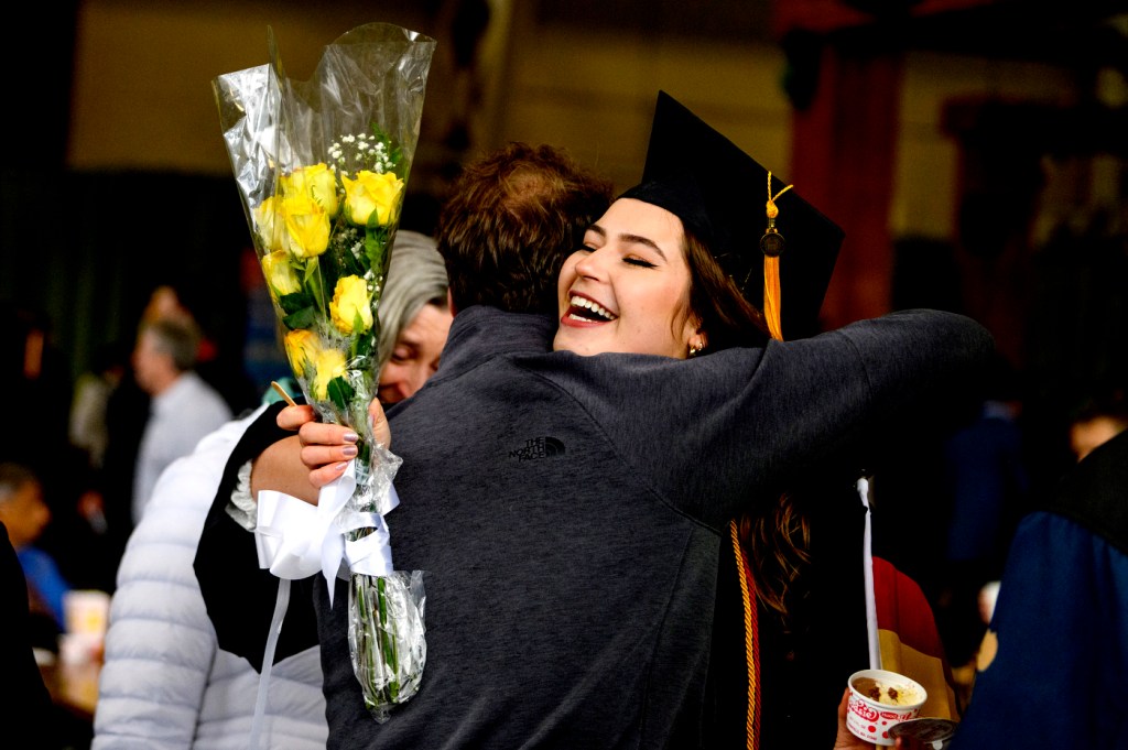 northeastern graduate holding yellow flowers hugging a family member