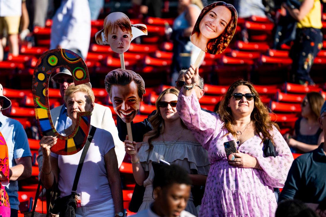 Family members in the stands at Fenway Park holding up cardboard cutouts of their graduates faces attached to wooden sticks.