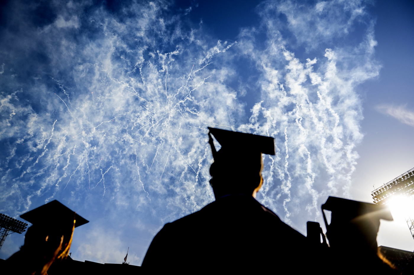 silhouette of graduates in commencement regalia looking up at fireworks