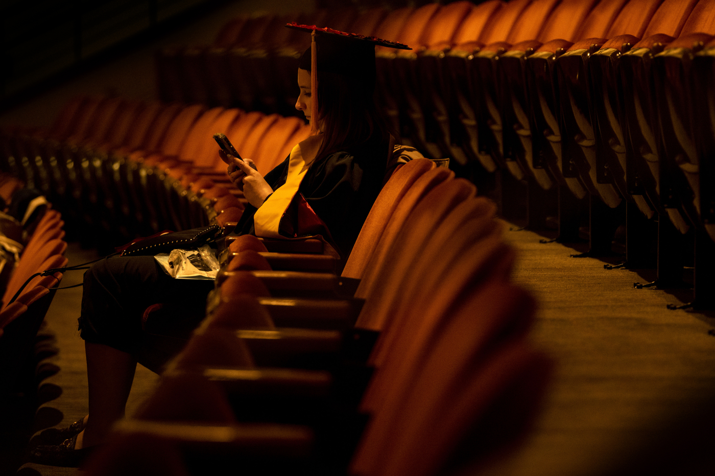 person in commencement regalia sitting in auditorium