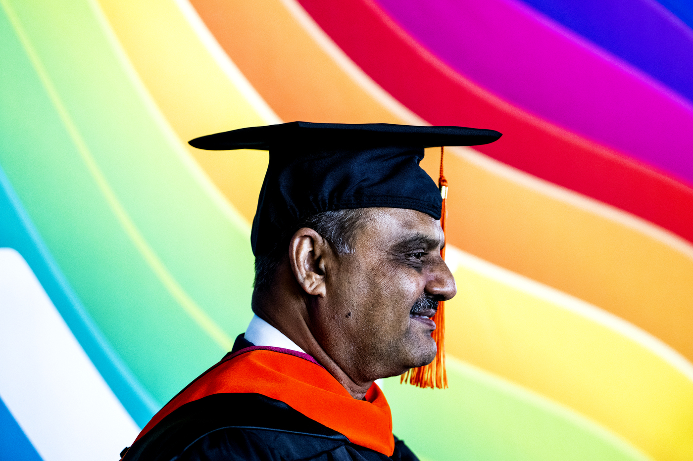 person wearing cap and gown on rainbow background