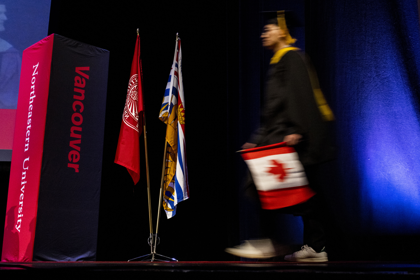 person carrying Canadian flag across stage at Vancouver convocation