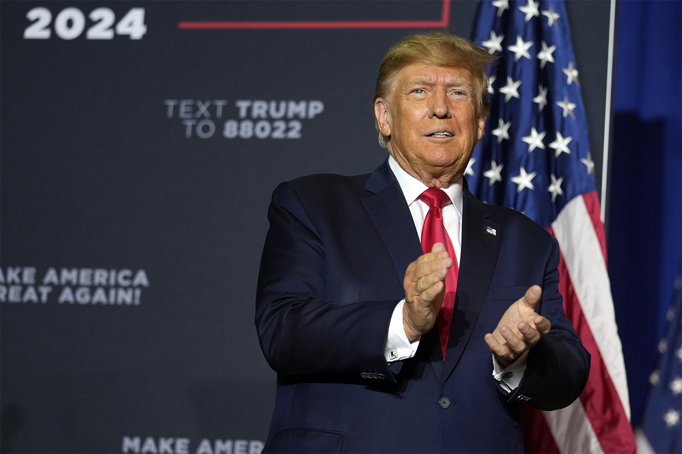 Trump clapping in front of 2024 campaign poster and US flag